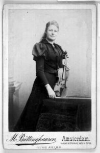 ヴァイオリニストのアマンダ・マイエルのポートレート。ヴァイオリンを左手に持ちつつ低めのテーブルに立てて、右手で弓をそのテーブルに置いているような構図で撮られた膝上の写真。