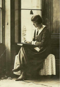 何かに腰掛け膝の上に置いた本の表紙の上で楽譜を書くハウエル